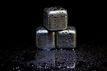Stainless steel cubes simulating ice for cooling drinks on a black surface with a reflection.