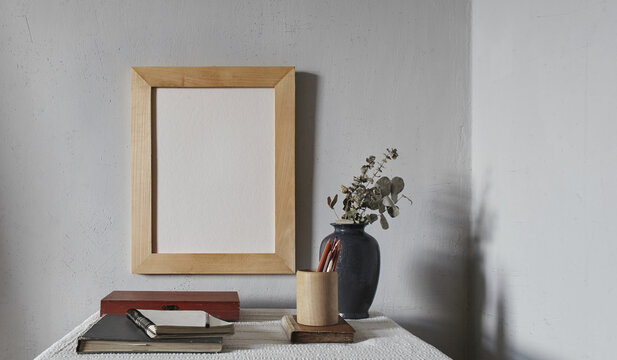 Wooden frame mockup. Scandinavian minimal design. Flowerpot on a pile of books on an old wooden desk. Composition on a white wall background