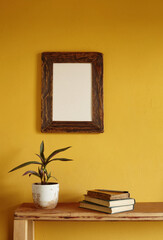 Wooden picture frame mockup. Flowerpot on a pile of books on an old wooden shelf. Composition on a yellow wall background