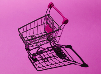 Shopping trolley on pink background with shadows. Mini shopping concept