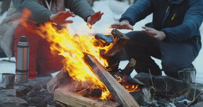 Friends camping in winter forest warming hands by fire