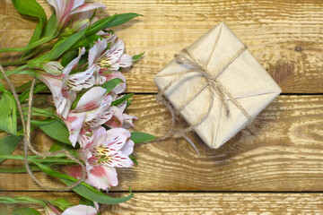 Bright white and pink flowers Alstroemeria and craft paper wrapped gift box on wooden textured background close-up