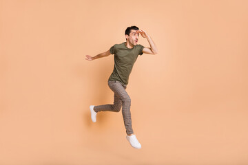 Fototapeta na wymiar Full length body size photo of jumping high man looking forward far hand near forehead isolated on pastel beige color background