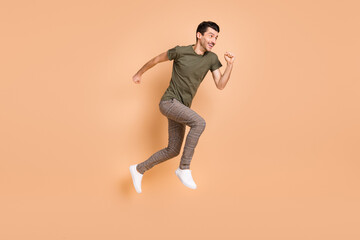 Fototapeta na wymiar Full size profile side photo of young happy cheerful excited man running fast in air isolated on beige color background