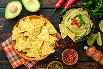 Guacamole. Traditional latinamerican Mexican dip sauce in a black bowl with avocado and ingredients and corn nachos. Avocado spread. Top view. Copyspace