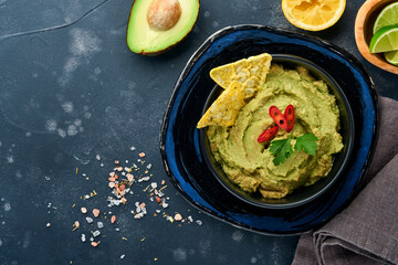 Guacamole. Traditional latinamerican Mexican dip sauce in a black bowl with avocado and ingredients and corn nachos. Avocado spread. Top view. Copyspace