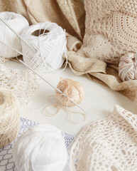 Cotton thread and hook on a table surrounded by cotton balls and doilies
