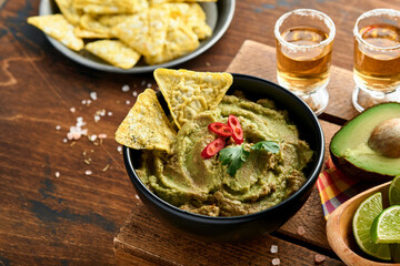 Guacamole. Traditional latinamerican Mexican dip sauce in a black bowl with avocado and ingredients and corn nachos. Avocado spread. Top view. Copyspace