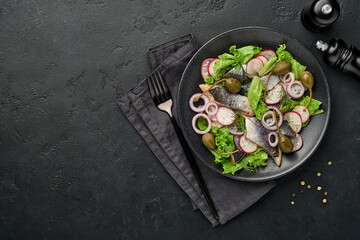 Salted herring with spice, capers, herbs and onion salad on black plate on dark background with copy space. Marinated sliced fish. Food with healthy unsaturated fats, flat lay