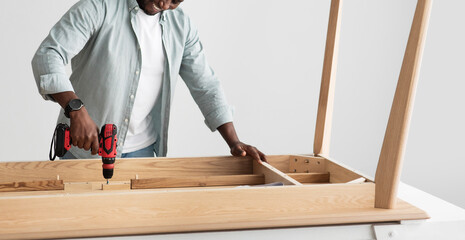 Experienced craftsman drilling wooden planks of table, assembling furniture with electric drill, panorama