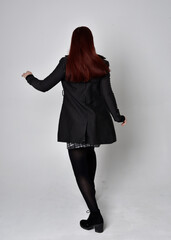 Full length portrait of a red haired  girl wearing black coat, tartan skirt and boots.  Standing...
