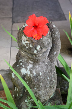 インドネシアのバリ島、ウブドの街角、頭に赤いハイビスカスの花を飾られた恐竜?トカゲ?の石像。
