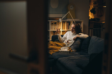 Naklejka premium depressed woman sitting on sofa and drinking alcohol. evening scene