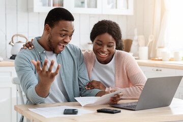 Excited black happy couple celebrating good news in kitchen, reading mail letter