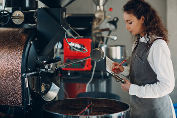 Coffee roaster machine and barista woman with tablet write pen at coffee roasting process