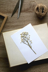 White paper with pressed gypsophila flowers and old book on a table. Making herbarium at home. Flat lay.