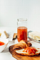 Breakfast with a fresh croissant and a cup of aromatic coffee latte, tangerine jam, butter and brie cheese. Fruit carving. Healthy breakfast.