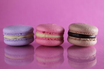 Obraz na płótnie Canvas Three macaroons lilac brown chocolate lavender pink lie in a row on a pink fuchsia-colored background with reflection and a place for text and copyspace