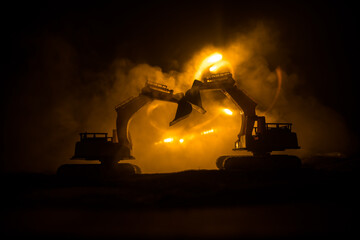 Construction site on a city street. A yellow digger excavator parked during the night on a construction site. Industrial concept table decoration on dark foggy toned background.