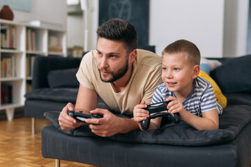 father playing video games with his son. they are sitting in living room