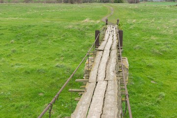 Fototapeta na wymiar Eearly spring landscape with ancient wooden foot-bridge through local meadow over small river Tomakivka in Topyla village, central Ukraine