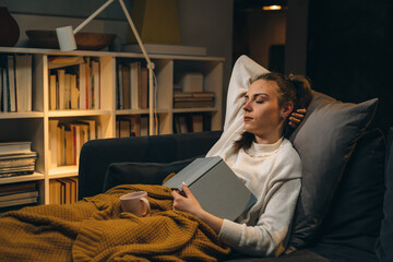 woman fall asleep why she was reading book. she is relaxed at sofa in her living room