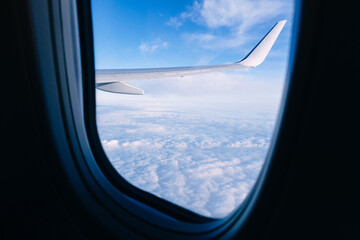 Fototapeta na wymiar An airplane wing looks out the airplane window with a clear sky and beautiful clouds with sunbeams