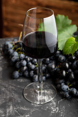 Wine glass with red wine on black table, dark wooden background. Red wine drink in glass with black grapes. Beaujolais Wine composition in cafe or restaurant