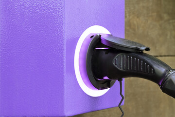 Electric car charger with purple electric car charging station on city street. Close up of power supply plugged into a power socket.