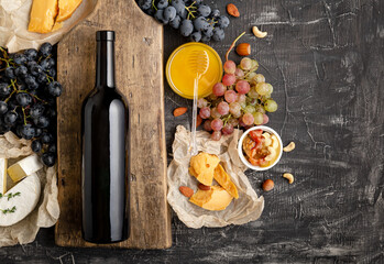 Wine and cheese composition. Red wine bottle mockup on vintage cutting wooden board. Gastronomy...