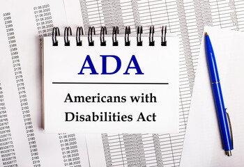 On the table are charts and reports, on which lie a blue pen and a notebook with the word ADA Americans with Disabilities Act