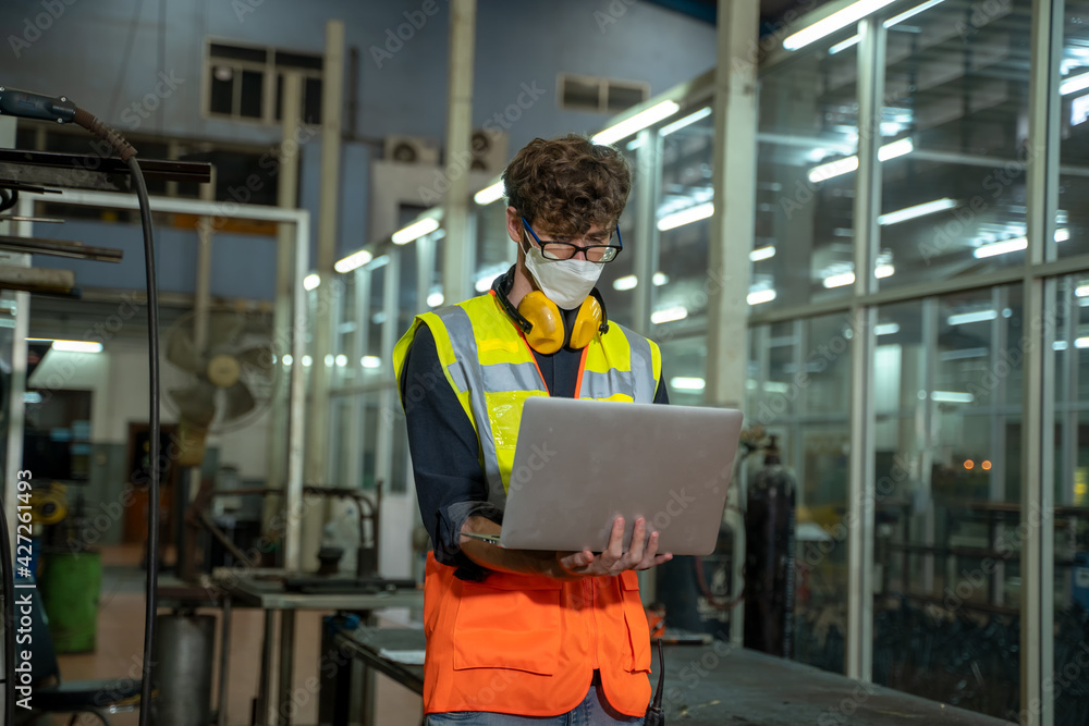 Poster professional technicians wears face mask standing and holding laptop with confident working at facto
