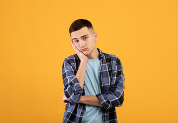 Portrait of young guy feeling bored, leaning on his hand, having dull day on orange studio...