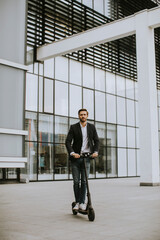 Young business man in a casual clothes riding an electric scooter by an office building on a business meeting