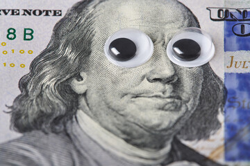 Fun Benjamin Franklin portrait with googly eyes, close-up of one hundred dollar bill.