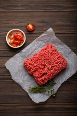Fresh raw minced meat from ground beef or pork with ingredients for cooking on cutting board and dark brown rustic wooden background from above 
