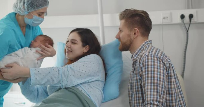 Young couple with doctor holding newborn baby in hospital ward