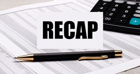The desktop contains reports, a calculator, a pen, and a white card with the text RECAP. Business...
