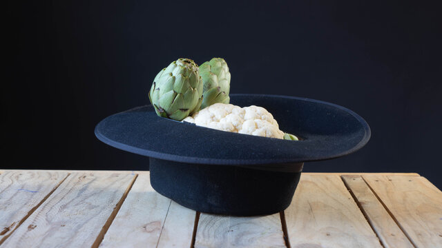 Alcachofas y coliflor en sombrero sobre mesa de madera