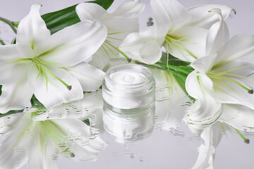 Obraz na płótnie Canvas Beauty jar cream cosmetic with lily flowers lie on table, jar cream product on wet flower mirror moistening. Natural flower jar cream cosmetics for hand skin care. Smooth beauty skin
