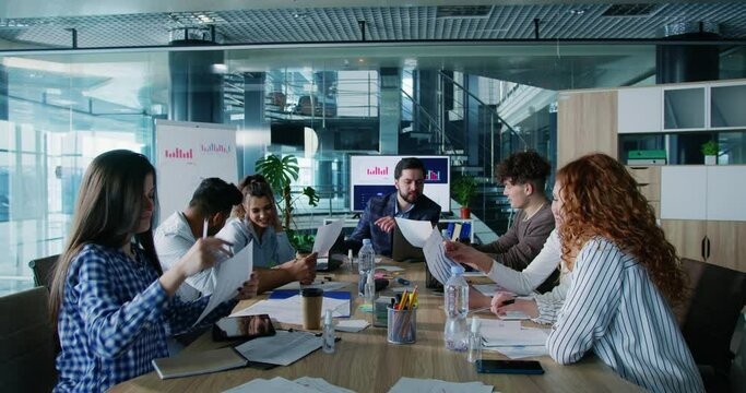 Group of multiethnic business people students sitting at conference table engaged in teamwork, enjoying professional internship seminar. Male mentor training corporate staff.