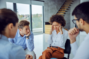 Upset businesswoman sitting in circle with support group and talking about problems. She is holding...