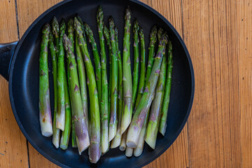 Fried green asparagus in black pan on wooden background. Top view, copy space.