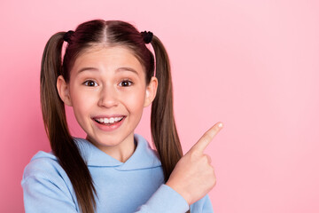 Photo portrait of small schoolgirl pointing finger blank space smiling isolated on pastel pink...