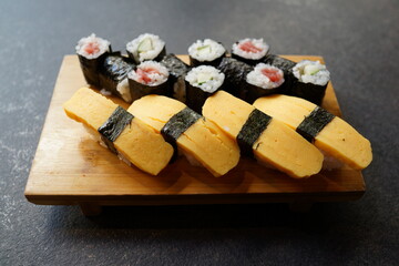 Tamago nigiri sushi and maki rolls with tuna and cucumber served on wooden board. Japanese food.