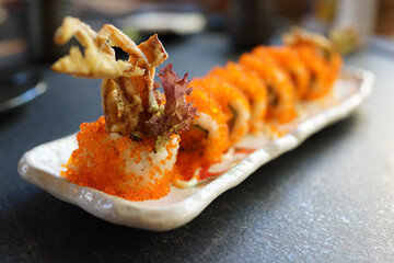 Sushi maki rolls California Futomaki with crispy soft shell crab, avocado, cucumber, crab and flying fish roe on a plate. Japanese traditional seafood served in a restaurant close-up. © ltyuan