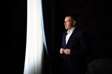 portrait of a man in a jacket by the window in a dark room.