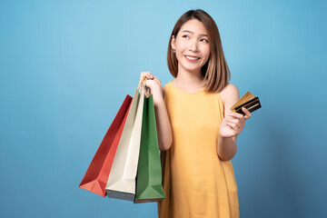 Fototapeta na wymiar Young asian woman carrying shopping bags and credit card, Isolated on blue background.