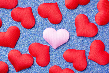 Pink decorative heart in the middle of many red hearts on blue sparkled background. Top view, close up, isolated.