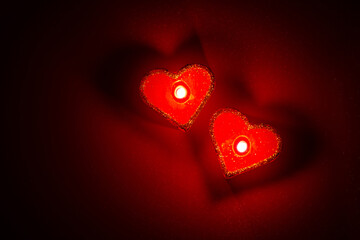 Heart shaped burning candles in dark red surrounding. Top view, isolated, close up.